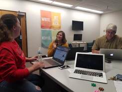 Three teachers interact around laptops